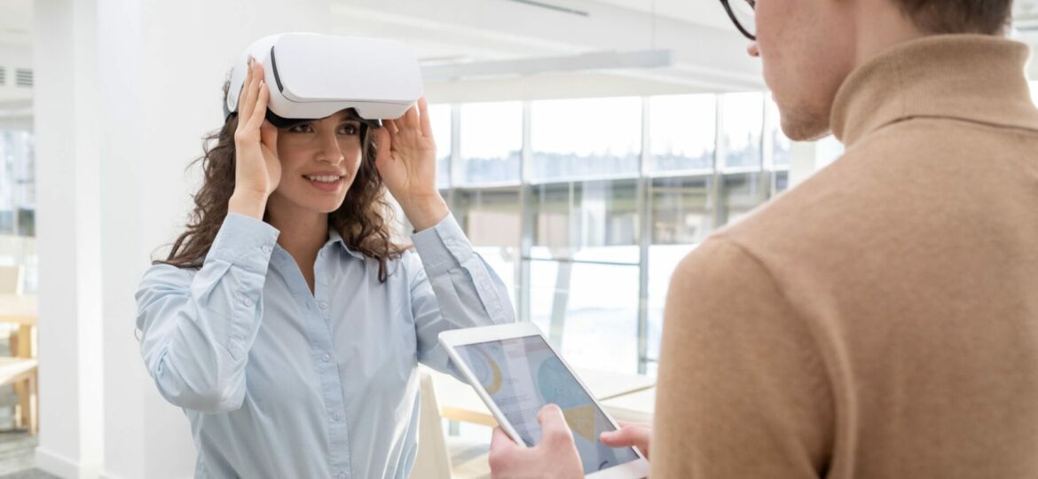 Happy young employee touching vr headset while communicating with male colleague