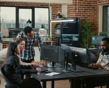 Junior dev programmers collaborating on group project compiling algorithm asking senior developer for help while intern joins the discussion. Software engineers brainstorming ideas looking at screens.