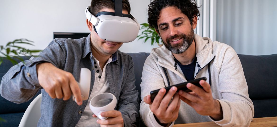 Caucasian men enjoying virtual reality glasses while sitting at table in home.