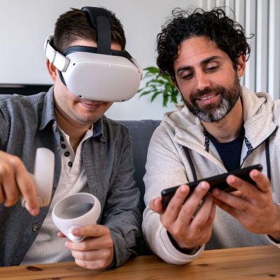 Caucasian men enjoying virtual reality glasses while sitting at table in home.