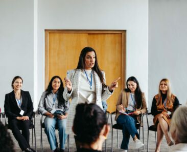 A female instructor is engaged in addressing a diverse group of people during a seminar in a bright conference room.