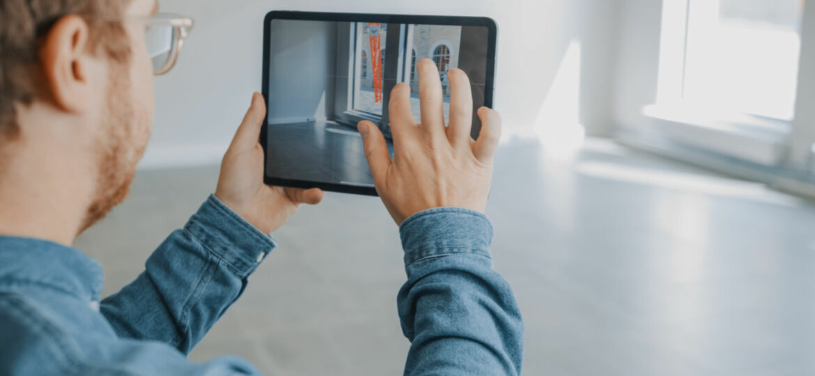 Young Hipster Man in Glasses Standing in Empty Office and Map it with an Augmented Reality Software on a Tablet Computer. Screen with Camera App.