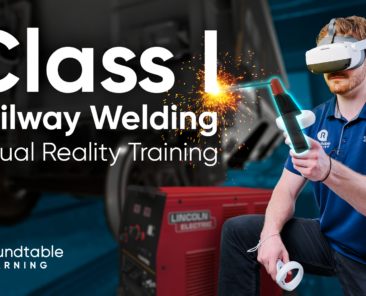 A welder wearing a VR headset practices a weld on the back of a virtual locomotive in a simulated rail yard environment.